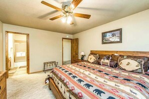 A bedroom with a bed, a ceiling fan, a painting, and a door leading to another room. - Paw's Cabin - Ockenden Ranch (Shaver Lake)