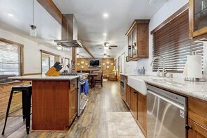 A modern kitchen with wooden cabinets, a stainless steel dishwasher, and a central island with bar stools. - Sparrow Cabin - East Village (Shaver Lake)