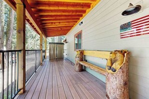 A covered wooden deck with a bench and a wall-mounted light fixture. - Sparrow Cabin - East Village (Shaver Lake)