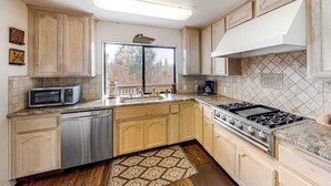 Une cuisine avec des meubles en bois, un lave-vaisselle en acier inoxydable, un four à micro-ondes, une cuisinière à gaz et un tapis à motifs.