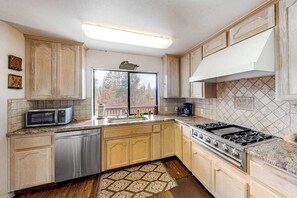 A kitchen with wooden cabinets, a stainless steel dishwasher, a microwave, a gas stove, and a patterned rug. - Forest With A View - Musick Falls (Shaver Lake)