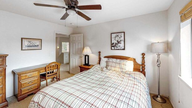 Une chambre à coucher comprenant un lit, un bureau, une chaise, un ventilateur de plafond, une lampe et une fenêtre.