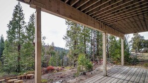 Une terrasse en bois offrant une vue sur un paysage naturel, entourée d’arbres et d’une zone boisée.