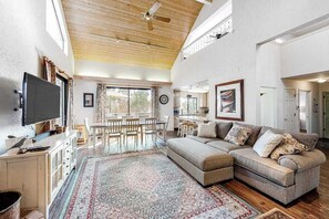 A spacious living area with a large sectional sofa, a dining table, and a television. - Forest With A View - Musick Falls (Shaver Lake)