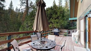 A deck with a round table and chairs, an umbrella, and a grill. - The Limit - West Village (Shaver Lake)