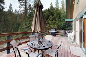 A deck with a round table and chairs, an umbrella, and a grill. - The Limit - West Village (Shaver Lake)
