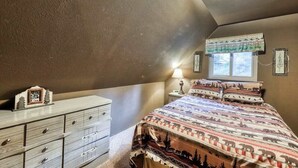 A bedroom with a bed, dresser, window, and a wall-mounted lamp. - The Limit - West Village (Shaver Lake)