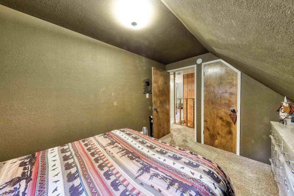 A bedroom with a sloped ceiling, a bed with a patterned bedspread, a dresser, and a door leading to another room.