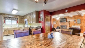 A dining area with a wooden table and chairs, a kitchen with wooden cabinets, and a fireplace. - The Limit - West Village (Shaver Lake)