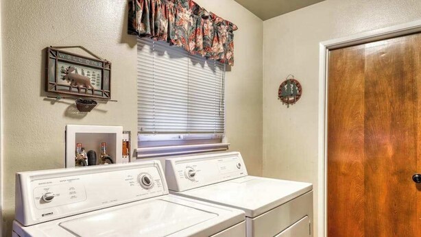 A laundry area with two front-loading washers and dryers, a window with blinds, a welcome sign, and a wooden door. - The Limit - West Village (Shaver Lake)