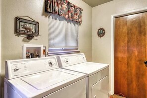 A laundry area with two front-loading washers and dryers, a window with blinds, a welcome sign, and a wooden door. - The Limit - West Village (Shaver Lake)