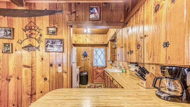 A wooden cabin interior with a kitchen area featuring a wooden countertop, a coffee maker, and a rustic decor. - Alpine Cottage - West Village (Shaver Lake)