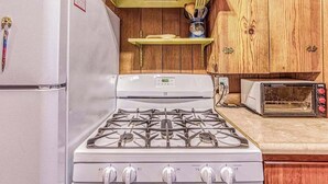 A kitchen with a gas stove, a toaster, and wooden cabinets. - Alpine Cottage - West Village (Shaver Lake)