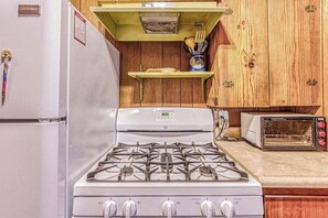 A kitchen with a gas stove, a toaster, and wooden cabinets. - Alpine Cottage - West Village (Shaver Lake)