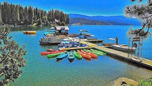 A lakeside dock with canoes, a small building, and a forested shoreline. - Alpine Cottage - West Village (Shaver Lake)