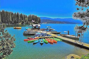 A lakeside dock with canoes, a small building, and a forested shoreline. - Alpine Cottage - West Village (Shaver Lake)