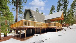 Uma cabana com um deck de madeira, uma janela grande e um chão coberto de neve.
