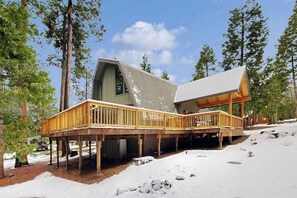 Eine Holzhütte mit einer Holzterrasse, einem großen Fenster und verschneitem Grund.