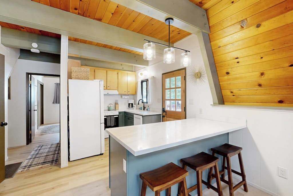 A modern kitchen with wooden ceiling beams, a central island with stools, and a view of the adjacent living area.