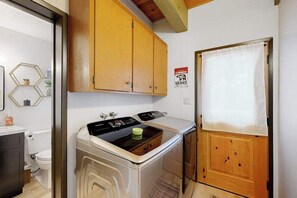 Cuina compacta amb rentadora i assecadora integrades, armaris de fusta i un senyal que indica avís d'os.