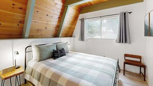 Um quarto com cama, mesa de cabeceira, um banco de madeira e uma janela com cortinas.