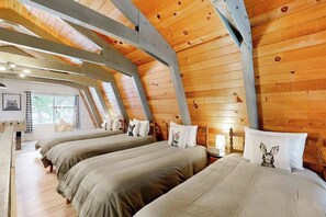 Ein Zimmer mit schrägen Wänden, Holztäfelung und drei Betten mit passendem Bettzeug.