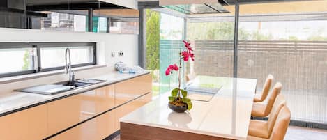 Una cocina moderna con una isla central, un comedor con mesa de vidrio y vistas a través de un amplio ventanal.