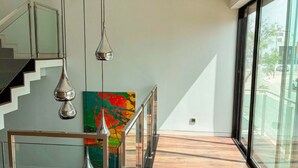 Et moderne interiør med trappe, glasgelændere og et stort vindue med udsigt til det fri.