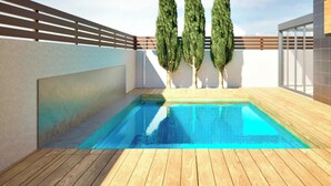 En swimmingpool med en træterrasse, omgivet af en lav mur og tre træer.