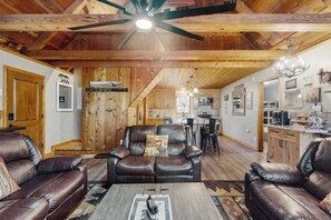 A spacious living room with leather sofas, a coffee table, and a ceiling fan. - Forest Edge Hideaway - Musick Meadows (Shaver Lake)