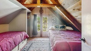 Ein Schlafzimmer mit zwei Betten, einem Fenster mit Vorhängen und einer Holzbalkendecke.