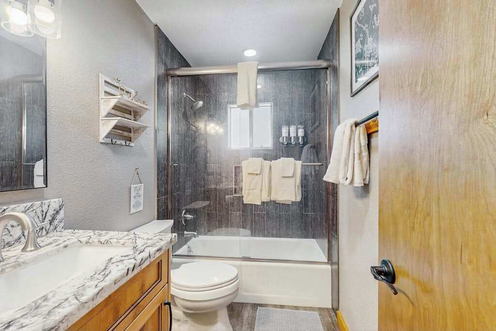 A modern bathroom with a marble sink, a toilet, a bathtub, and a shower enclosure.