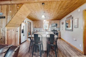 A kitchen with a central island, wooden cabinets, and a dining area with chairs. - Forest Edge Hideaway - Musick Meadows (Shaver Lake)