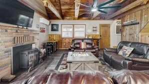 Ein gemütliches Wohnzimmer mit Kamin, Ledersofas, einem Flachbildfernseher und Holzbalken an der Decke.