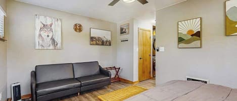 Une pièce comprenant un lit, un canapé, un ventilateur de plafond et des œuvres d’art accrochées aux murs.