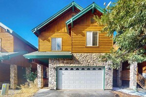 Eine zweistöckige Blockhütte mit Steinunterbau, Garage und begrüntem Dach.