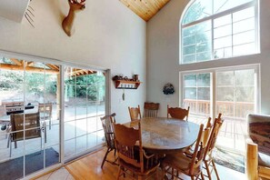 A dining area with a round table and wooden chairs, large windows, and a view of the outdoors. - Papa's Mountain Retreat - Shaver Lake (Shaver Lake)