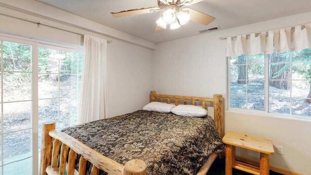 Een slaapkamer met een houten bed, een plafondventilator en grote ramen.