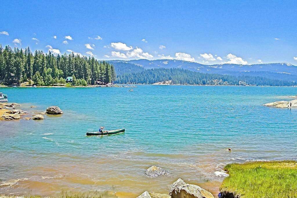 Un lago tranquilo con una canoa en primer plano, rodeado de costas rocosas y un bosque denso.