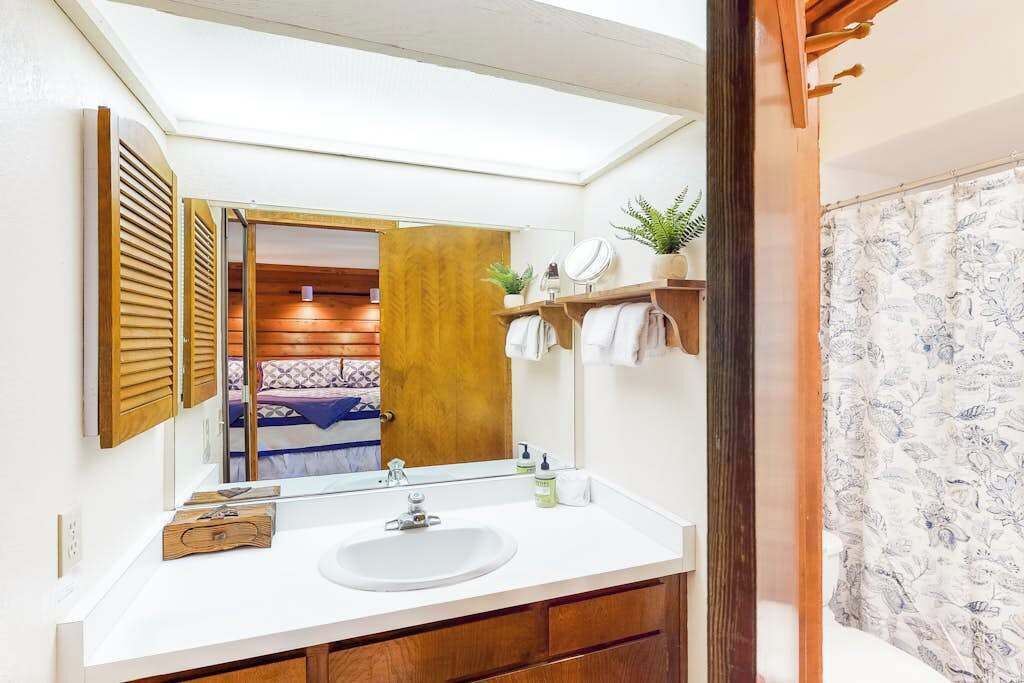 Een badkamer met een witte wastafel, houten kastjes, een spiegel en een douchegordijn met een bloemenprint.