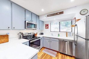 A modern kitchen with stainless steel appliances, a coffee sign, and a window providing natural light.