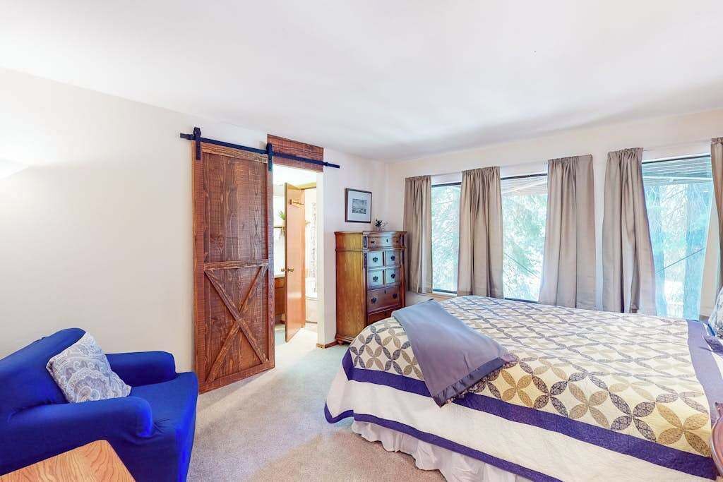 A bedroom with a bed, a blue armchair, a wooden wardrobe, and a dresser.