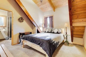 A bedroom with a sloped ceiling, a bed with a patterned bedspread, a bedside table with a lamp, and a window with curtains. - Majestic Mountain - Big Trees Village (Dorrington)