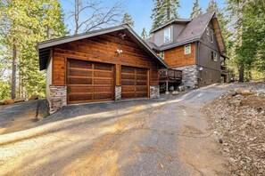 Eine zweistöckige Holzhütte mit Steinunterbau, eine Garage mit zwei Stellplätzen und eine Auffahrt zur Einfahrt.