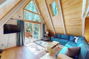 A spacious loft-style room with a large window, a flat-screen TV, a sofa, and a coffee table. - Big Trees Getaway - Big Trees Village (Dorrington)