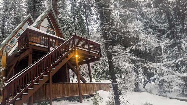 En træhytte med en trappe op til en balkon, omgivet af sneklædte træer.