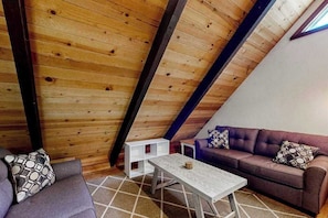 Une chambre à coucher confortable, aménagée en mezzanine, avec un plafond en pente, un canapé, une table basse et un coussin à motifs.
