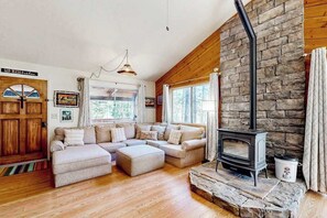 Ein gemütliches Wohnzimmer mit Kamin aus Stein, Holzbalken und einem großen Fenster.