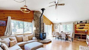 Un acogedor interior de cabaña con chimenea de piedra, paredes de madera, un conjunto de sofás y una zona de comedor.