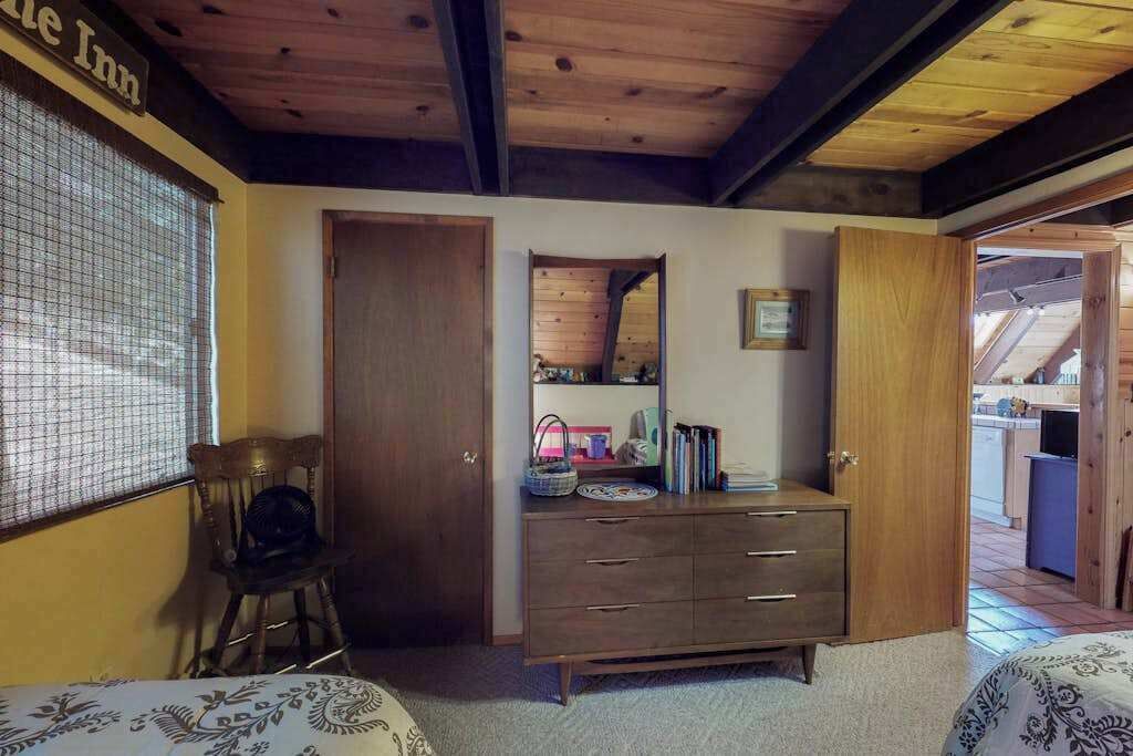 Een slaapkamer met een houten plafond, een dressoir met lades, een stoel en een bed met beddengoed met dessin.